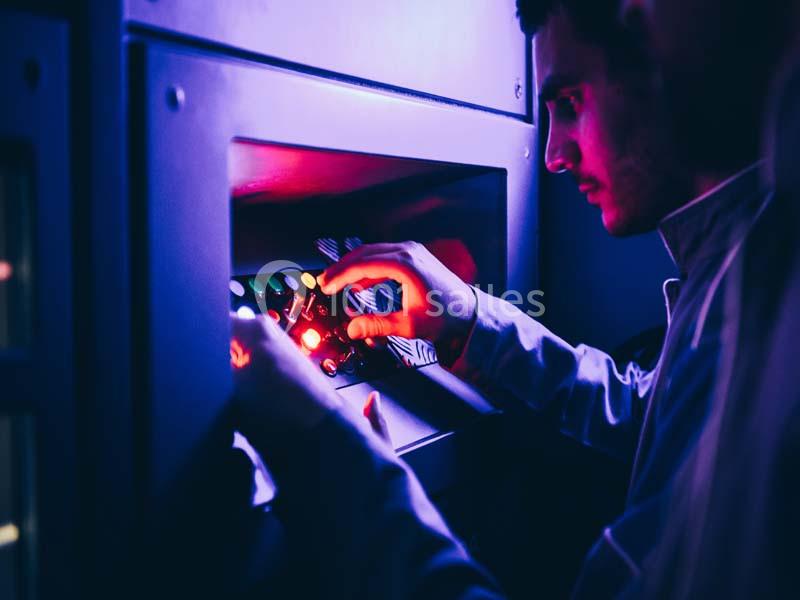 Un homme manipule des commandes lumineuses sur un panneau de contrôle dans une ambiance éclairée en violet.