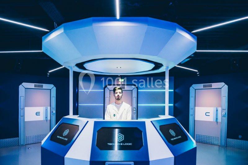 Un homme se tient derrière un comptoir futuriste dans une pièce éclairée par des néons bleus.