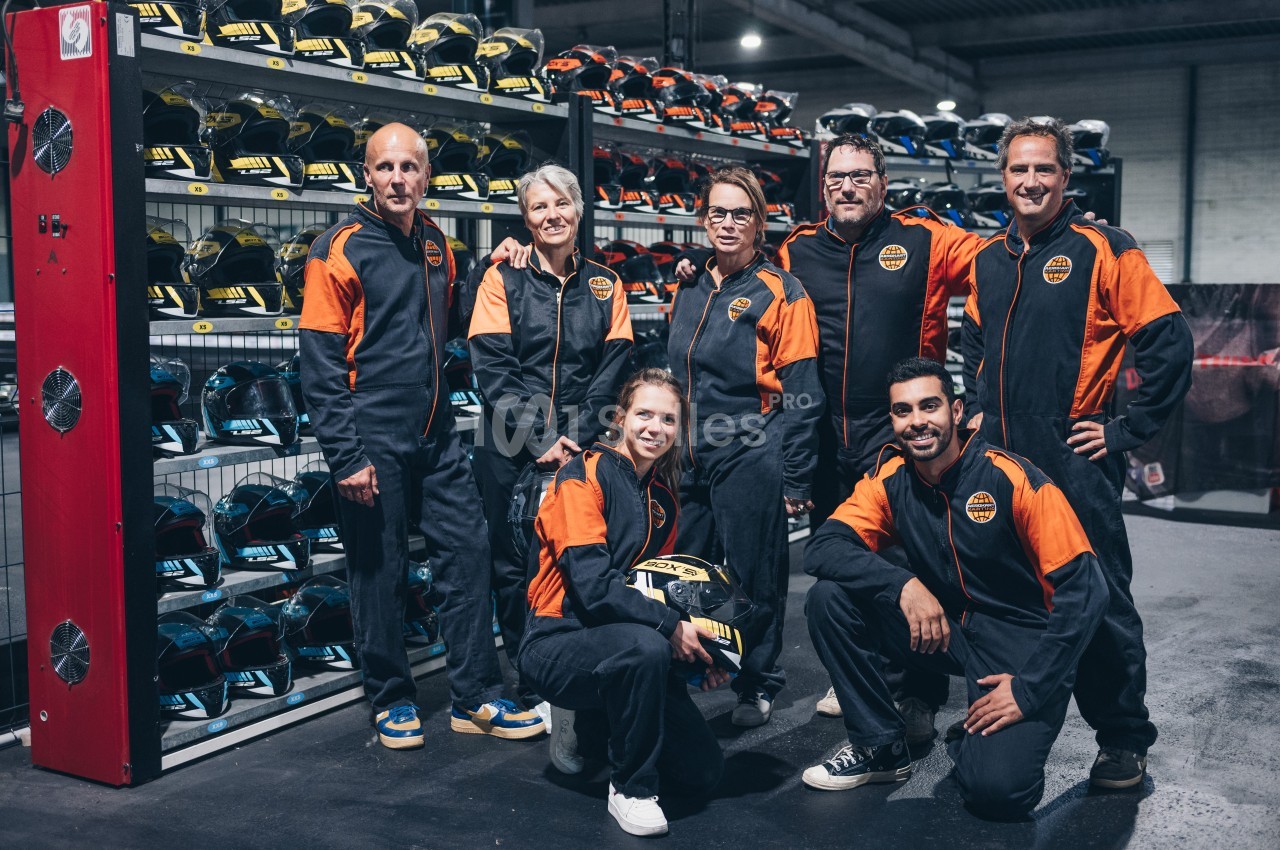 Un groupe de personnes en tenue de karting posant devant des étagères remplies de casques colorés.