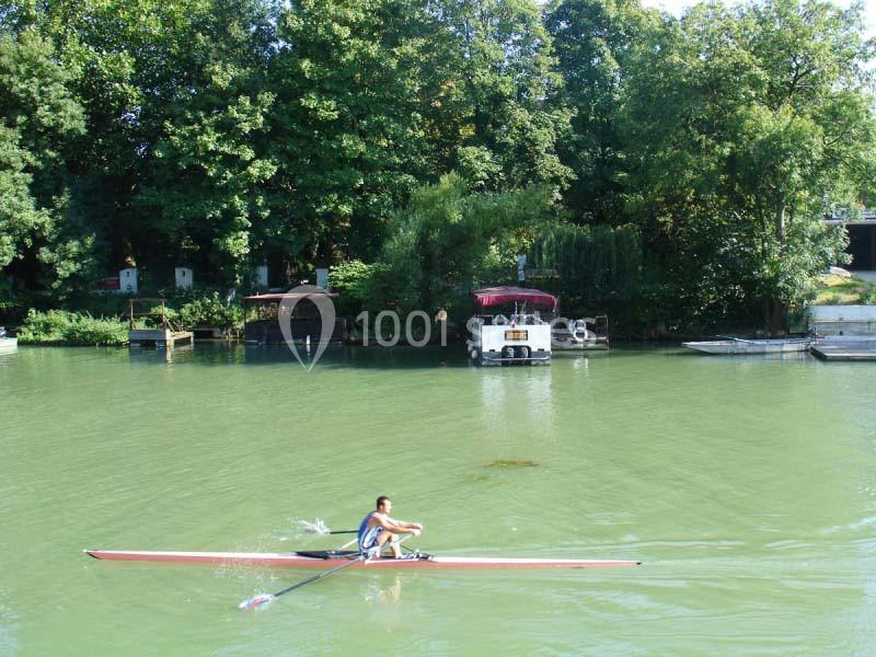 Un rameur seul sur une rivière calme, entourée d'arbres et de petites structures au bord de l'eau.