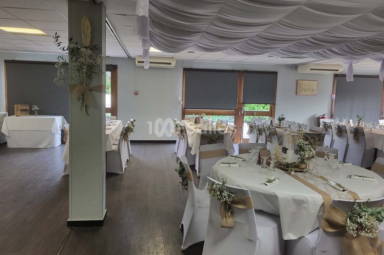 Salle de réception décorée pour un événement, avec tables dressées, chaises blanches et ornements floraux.