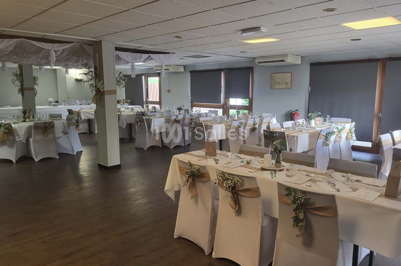 Salle de réception décorée pour un événement, avec tables dressées, nappes blanches et ornements floraux.