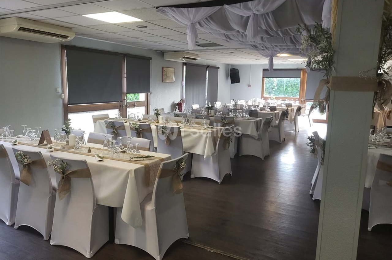 Salle de réception décorée avec des tables dressées, nappes blanches, chaises ornées et plafond drapé de tissu blanc.