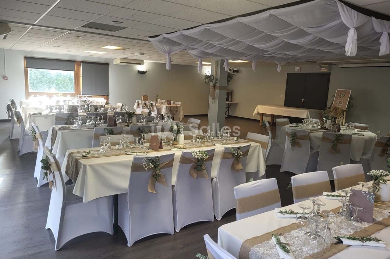 Salle de réception décorée pour un événement, avec tables dressées, nappes blanches et ornements floraux.