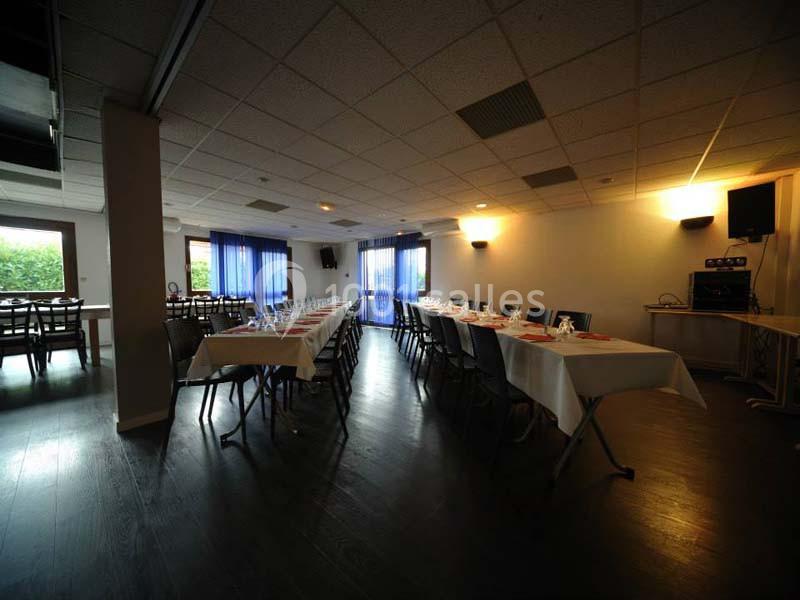 Salle de réception avec tables dressées, chaises alignées et grandes fenêtres laissant entrer la lumière naturelle.