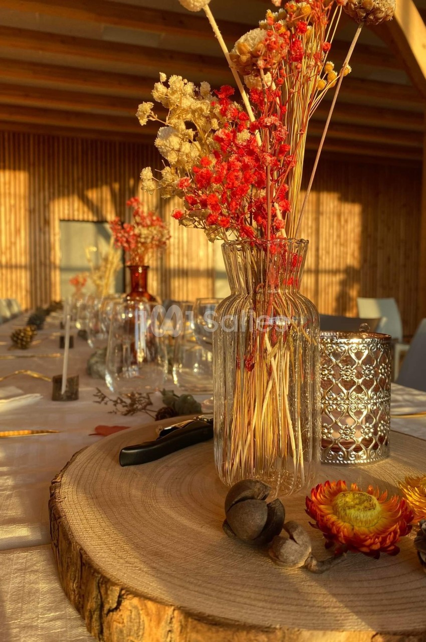 Centre de table automnal avec fleurs séchées dans un vase en verre, bougie décorative et rondin de bois.
