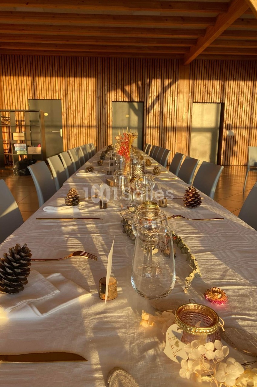 Table décorée pour un repas, ornée de pommes de pin, bougies et éléments naturels, dans une salle en bois éclairée par le…