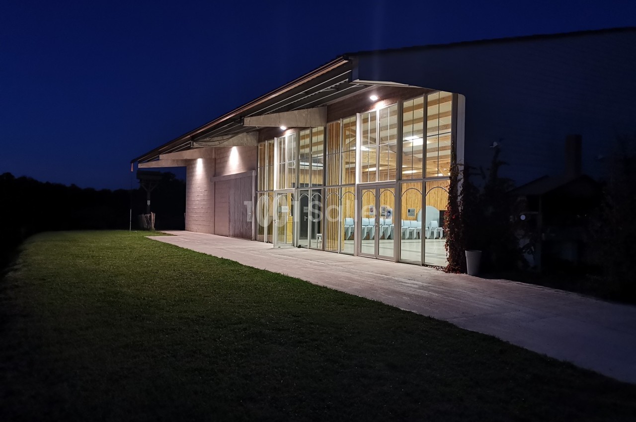 Bâtiment moderne avec façade vitrée illuminée, entouré d'une pelouse, photographié à la tombée de la nuit.