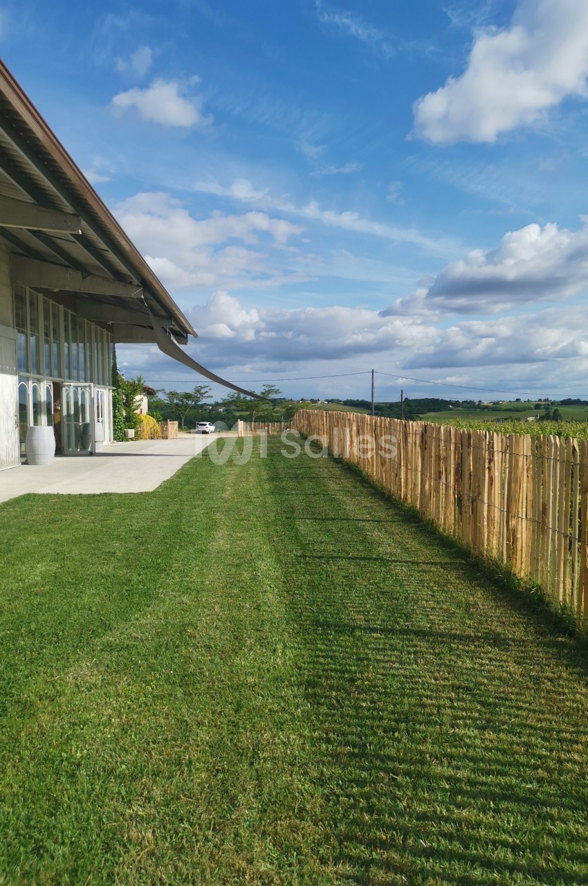Pelouse bien entretenue longeant un bâtiment moderne avec une clôture en bois et un paysage rural en arrière-plan.