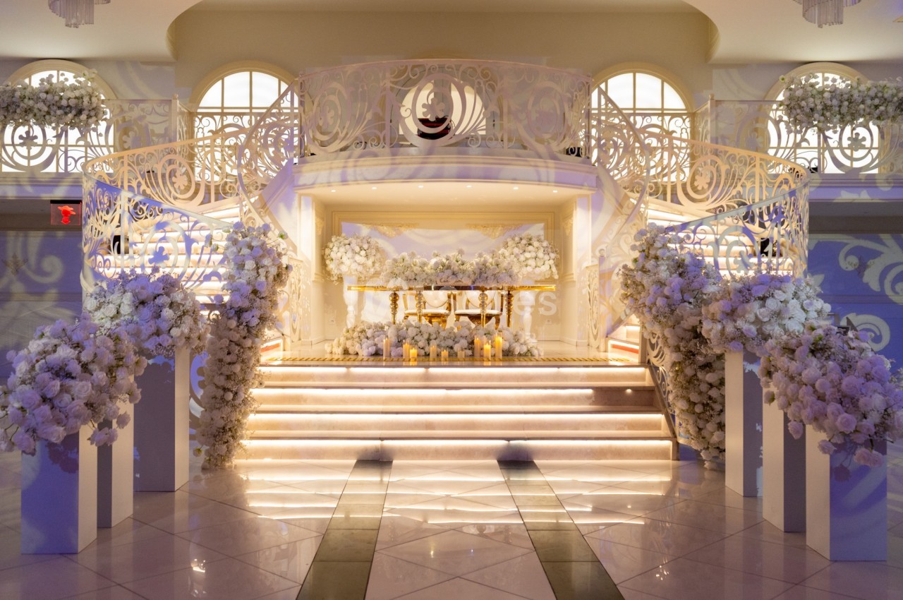 Escalier décoré de fleurs blanches menant à une estrade ornée de bouquets et de bougies dans une salle élégante.
