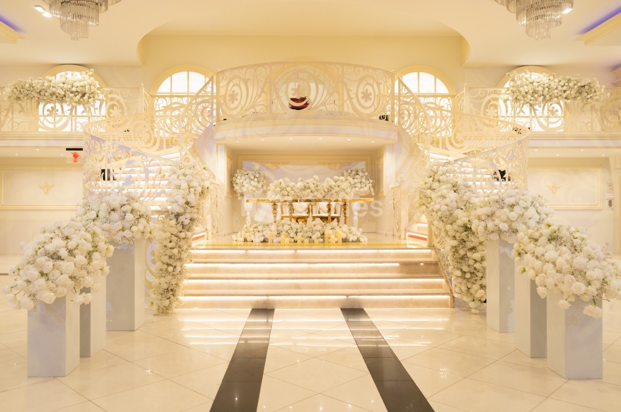 Escalier décoré de fleurs blanches menant à une scène ornée dans une salle lumineuse et élégante.