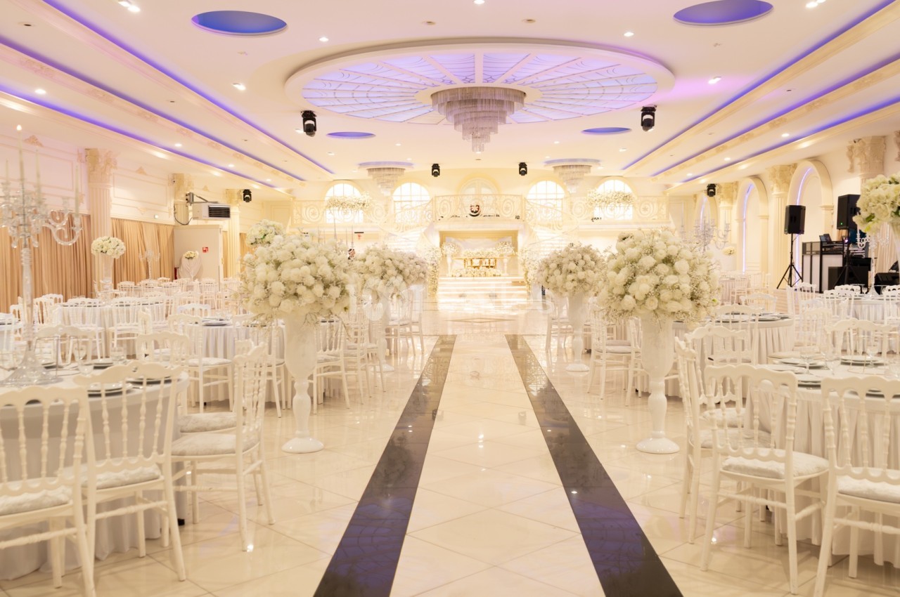 Salle de réception élégante avec tables rondes, chaises blanches et décorations florales blanches sous un éclairage…