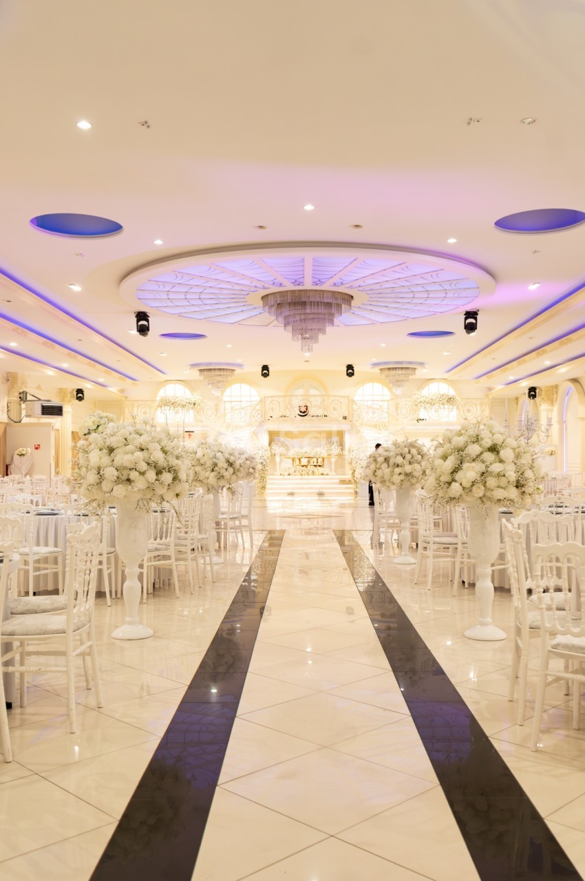 Salle de réception élégante avec décoration blanche, tables dressées et éclairage tamisé sous un plafond orné.