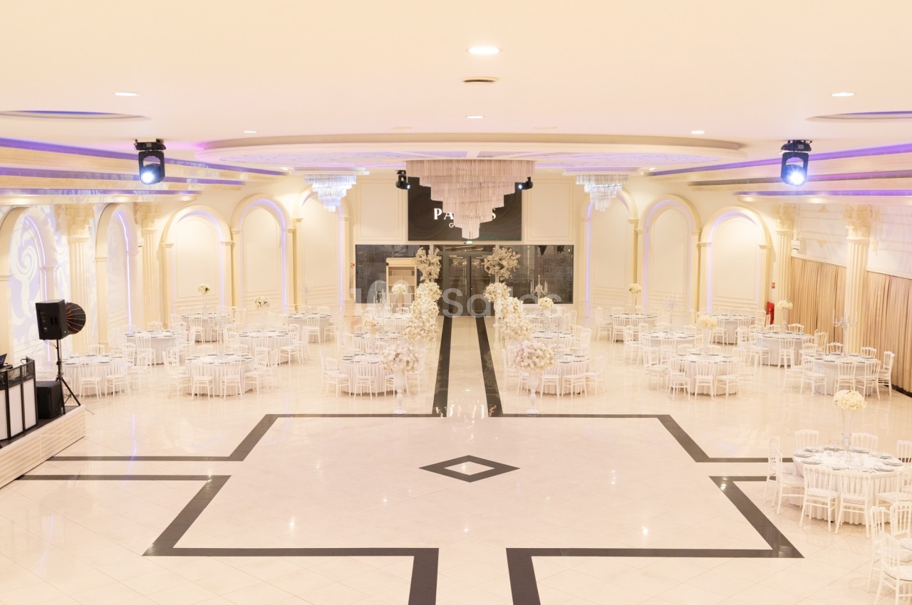 Salle de réception spacieuse avec tables rondes dressées, décorations élégantes et éclairage chaleureux.