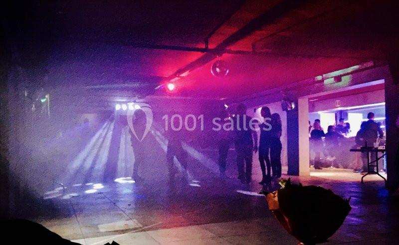 Des personnes dans une salle sombre avec des lumières colorées et de la fumée, ambiance de fête ou de soirée.