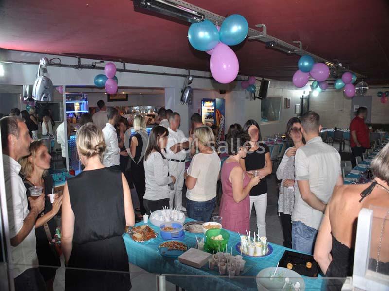 Groupe de personnes discutant autour d'une table garnie de plats dans une salle décorée de ballons colorés.