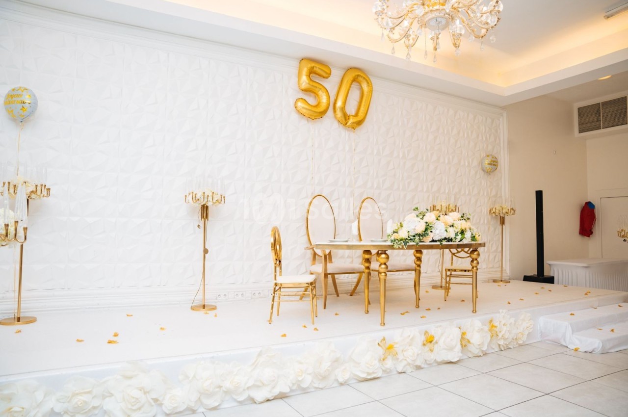Salle décorée pour une célébration avec une table ornée de fleurs blanches et des ballons dorés formant le chiffre 50.
