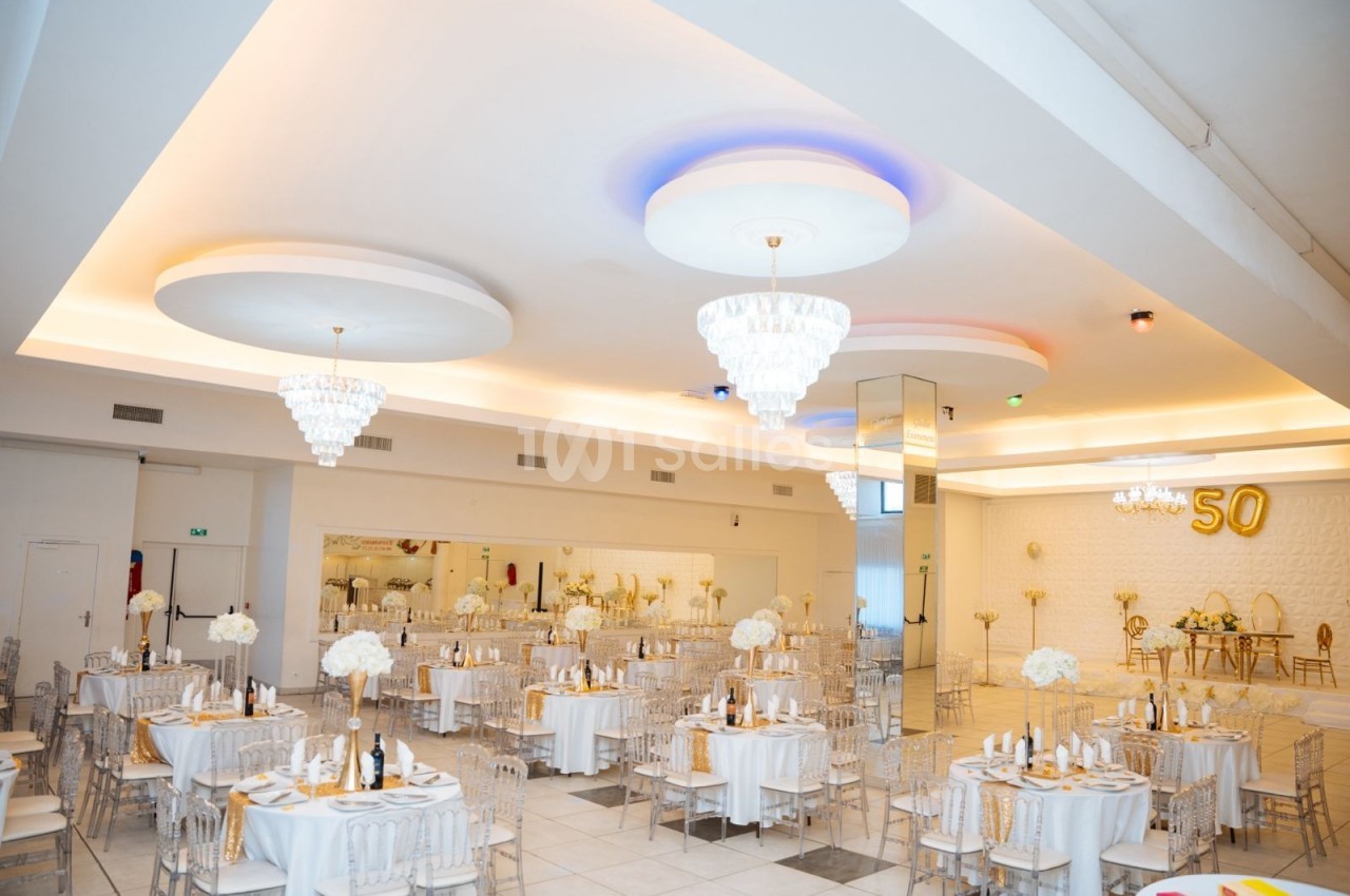 Salle de réception élégante décorée en blanc et or avec tables dressées, chandeliers et chiffre 50 en arrière-plan.