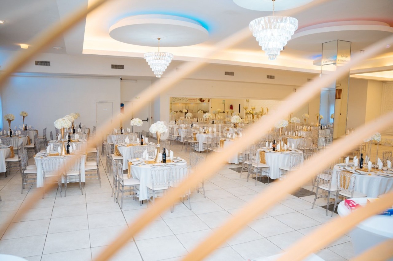 Salle de réception élégante avec tables dressées, décorations florales blanches et lustres suspendus.