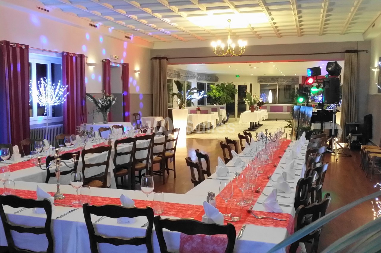 Salle de réception décorée avec des tables dressées, nappes blanches, chemins de table rouges et éclairages festifs.