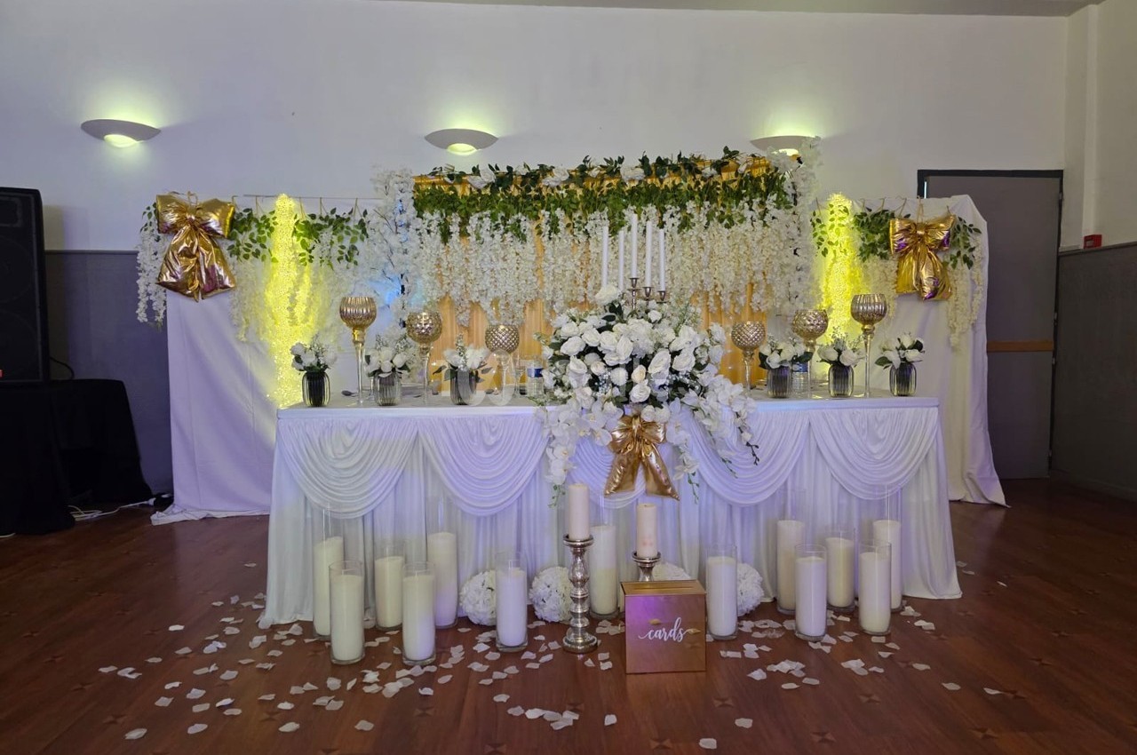 Table décorée pour un mariage avec fleurs blanches, chandeliers, guirlandes lumineuses et bougies sur un sol en bois.