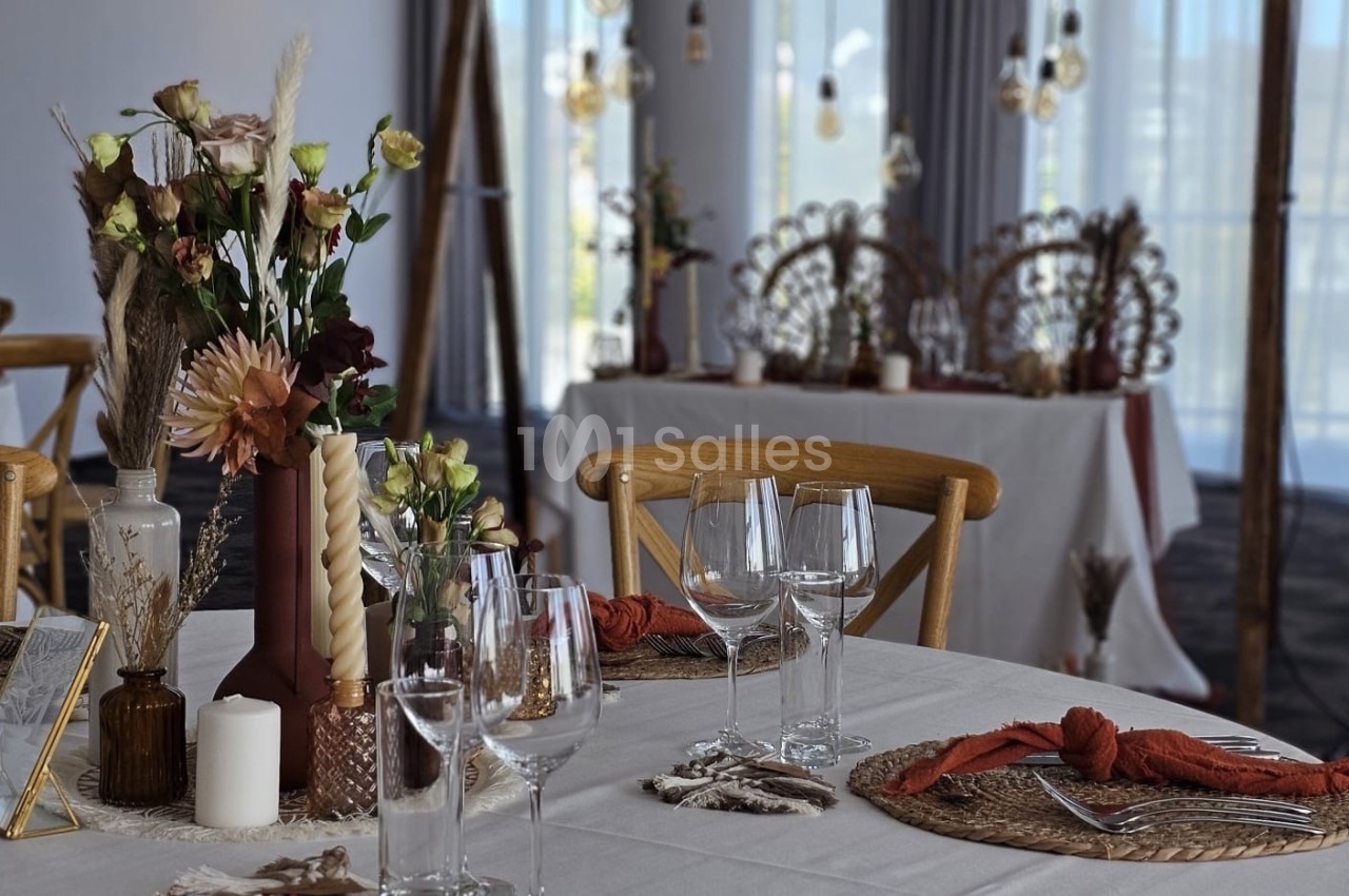 Table décorée avec des fleurs séchées, bougies et vaisselle élégante dans une salle lumineuse avec des tables en arrière…