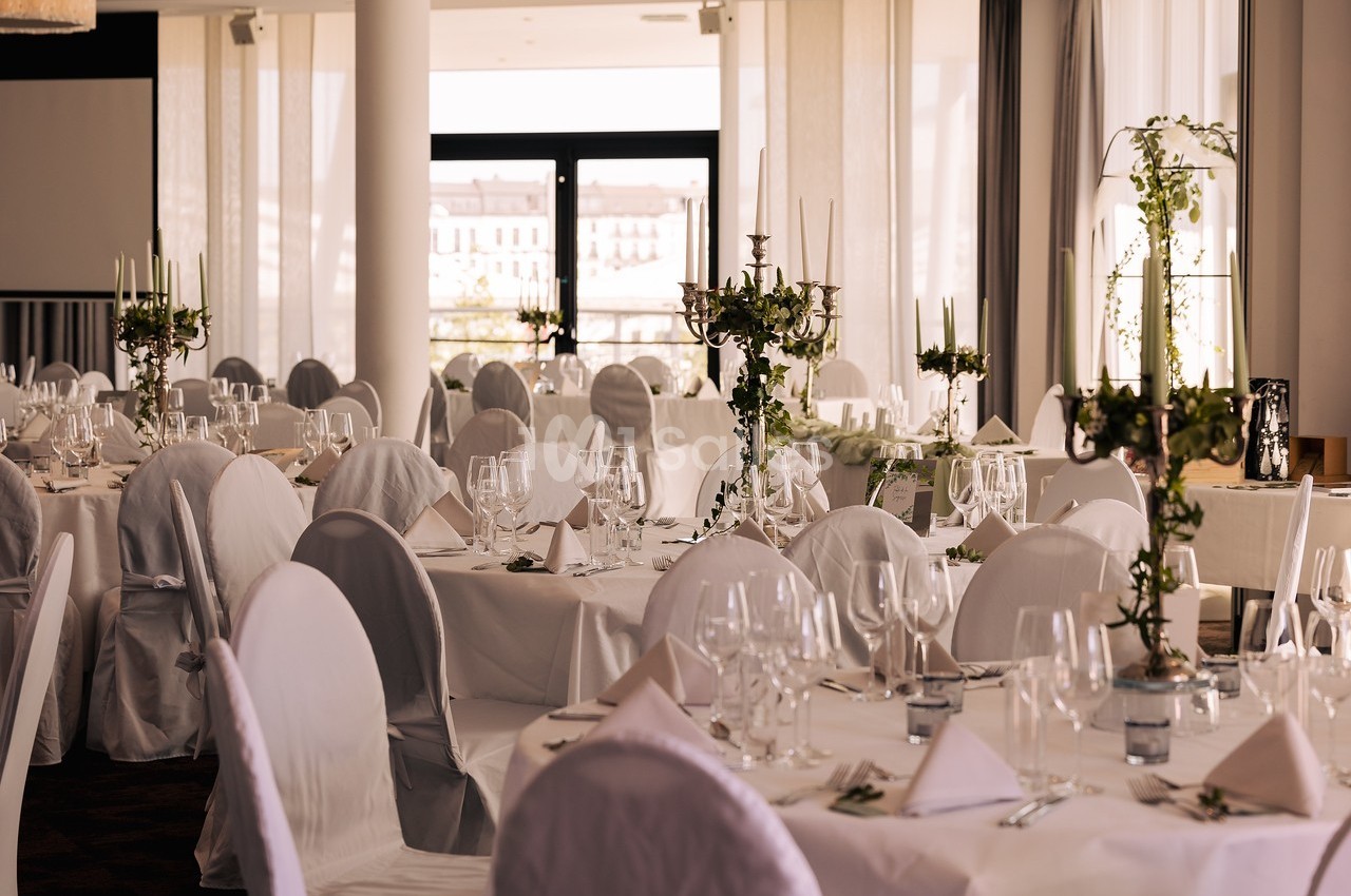 Salle de réception élégante avec tables dressées, nappes blanches, chandeliers et lumière naturelle.