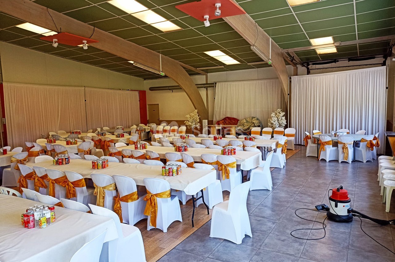 Salle de réception décorée avec des tables et chaises blanches ornées de nœuds orange, prête pour un événement.