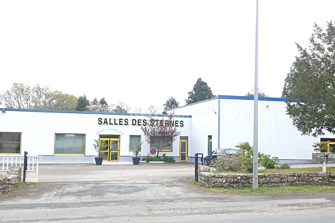 Bâtiment blanc avec enseigne ’Salles des Sternes’, entouré d'arbres et d'un parking à l'avant.