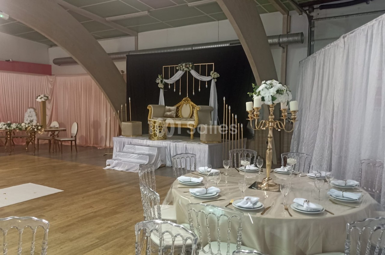 Salle de réception décorée avec des tables dressées, un canapé doré sur une estrade et des rideaux blancs en arrière-plan.