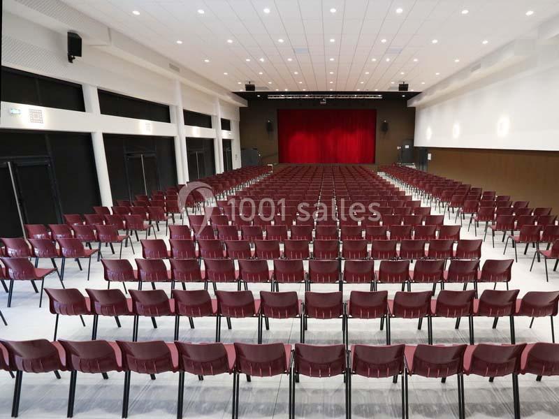 Salle de spectacle avec des rangées de chaises rouges alignées face à une scène avec un rideau rouge fermé.