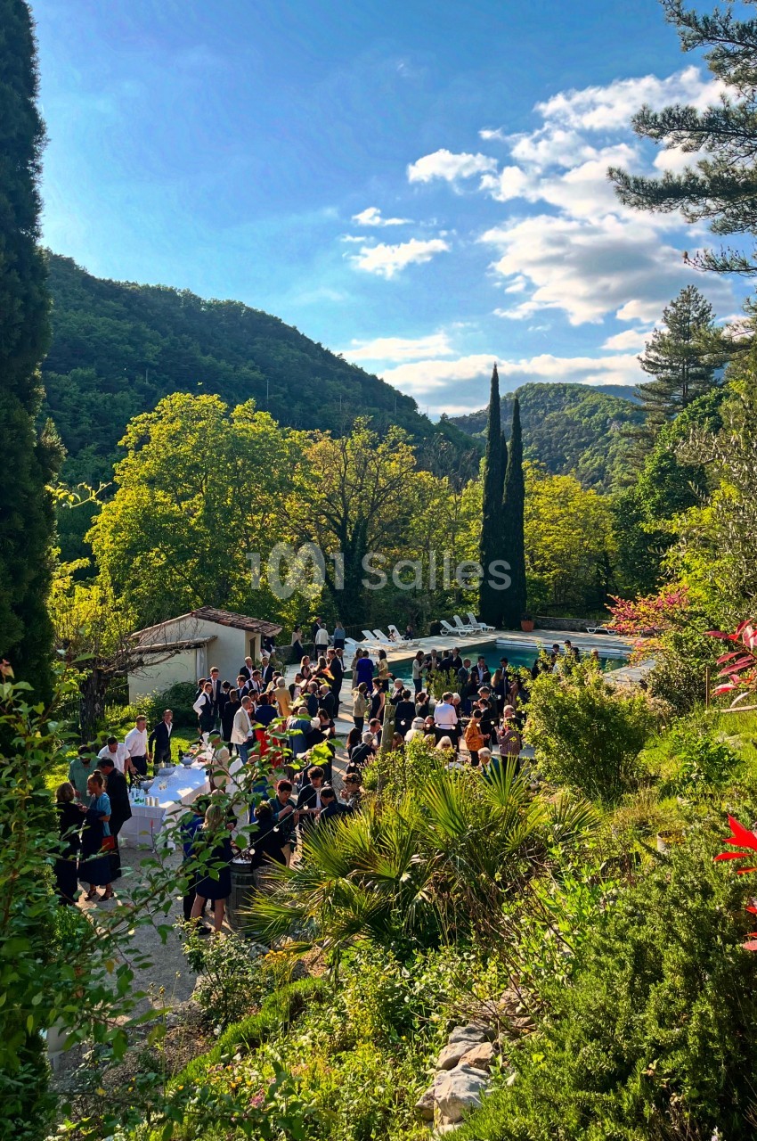 Groupe de personnes rassemblées dans un jardin verdoyant près d'une piscine, entouré de collines boisées.