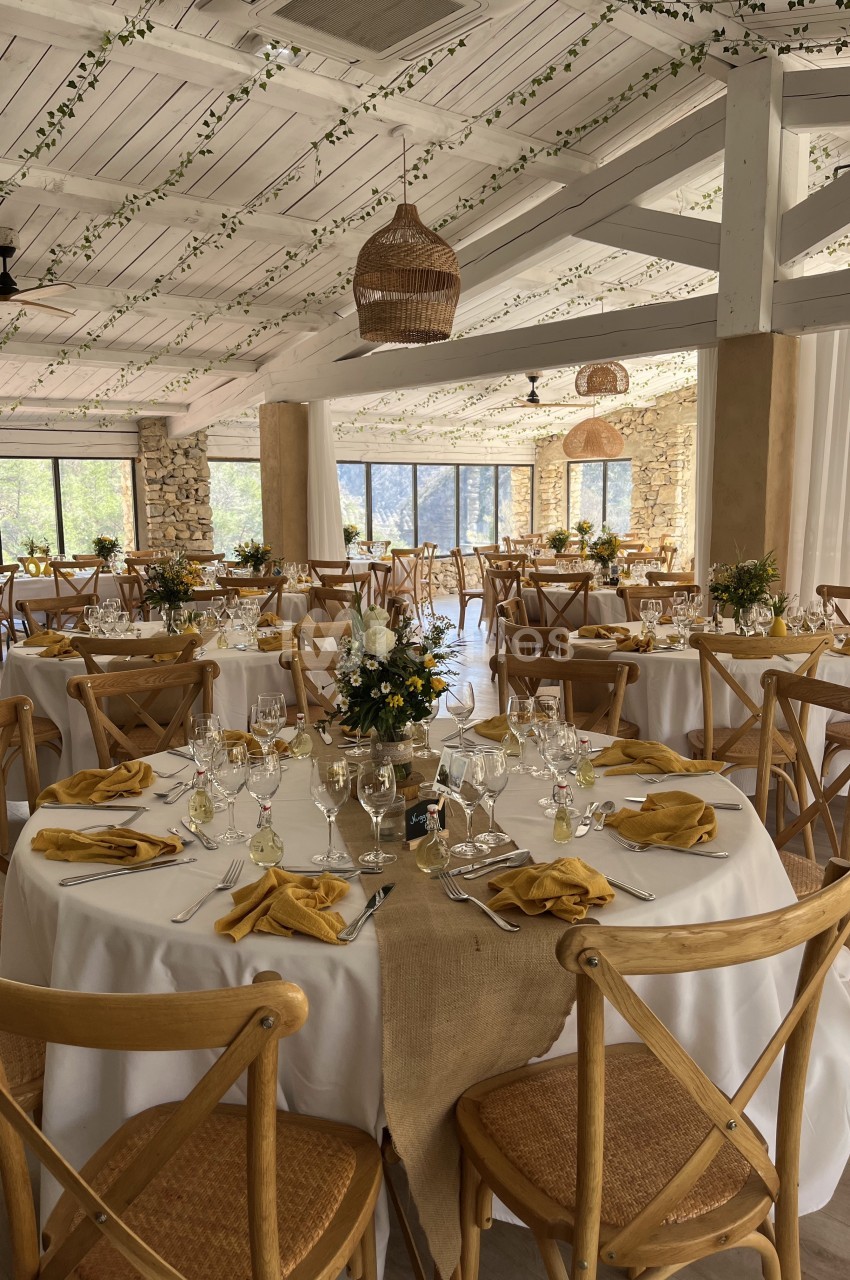Salle de réception décorée avec des tables rondes, nappes blanches, serviettes jaunes et arrangements floraux.