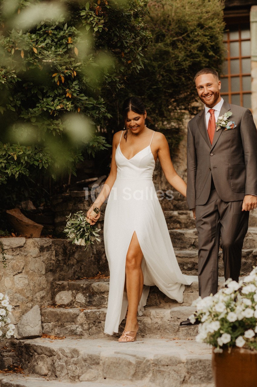 Un couple souriant descend des marches en pierre, la femme en robe blanche et l'homme en costume gris.