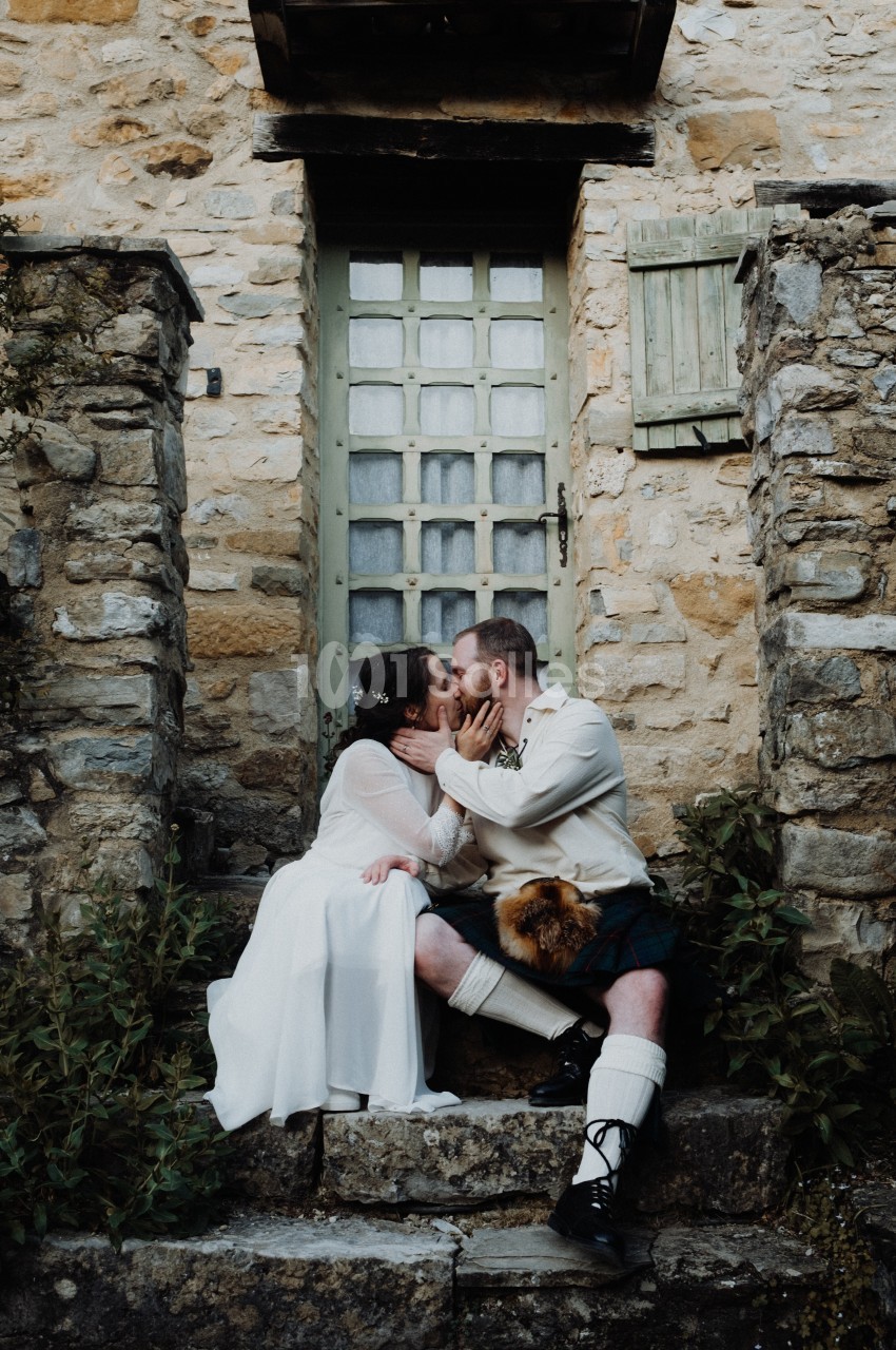 Un couple en tenue traditionnelle s'embrasse sur les marches d'une maison en pierre avec une porte vitrée.