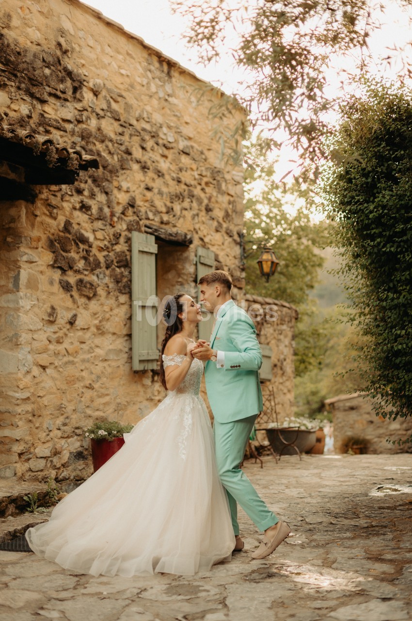 Un couple en tenue de mariage danse dans une ruelle pavée bordée de murs en pierre et de verdure.