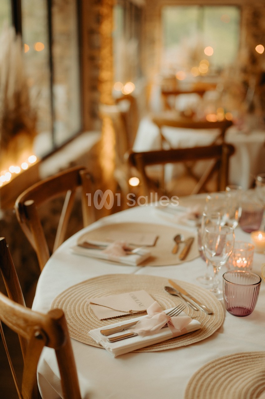 Table dressée avec élégance, comprenant assiettes, couverts, serviettes nouées et verres, dans une ambiance chaleureuse.