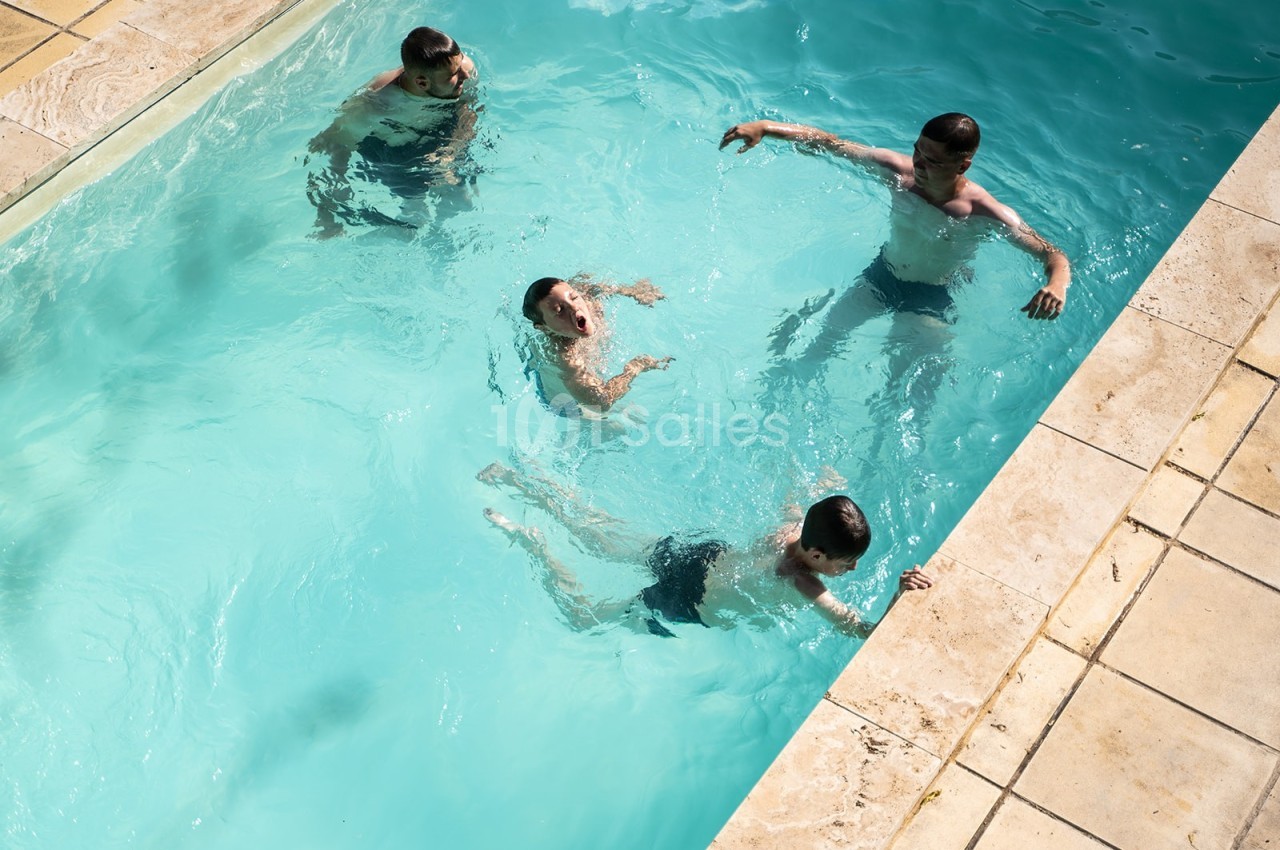 Quatre personnes nagent et jouent dans une piscine extérieure entourée de margelles en pierre.