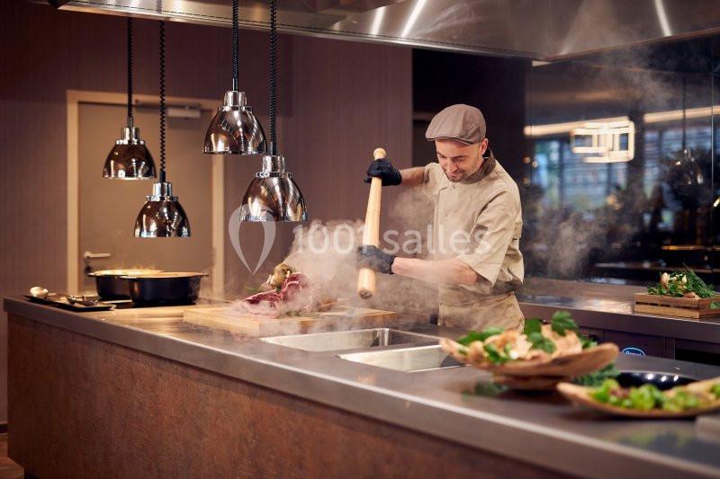 Un cuisinier prépare un plat chaud dans une cuisine professionnelle sous des lampes suspendues.