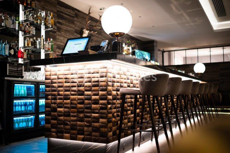 Bar moderne avec comptoir éclairé, tabourets hauts, étagères de bouteilles et ambiance tamisée.