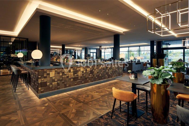 Bar moderne avec comptoir en bois texturé, éclairage chaleureux, tables et chaises design dans un espace spacieux.