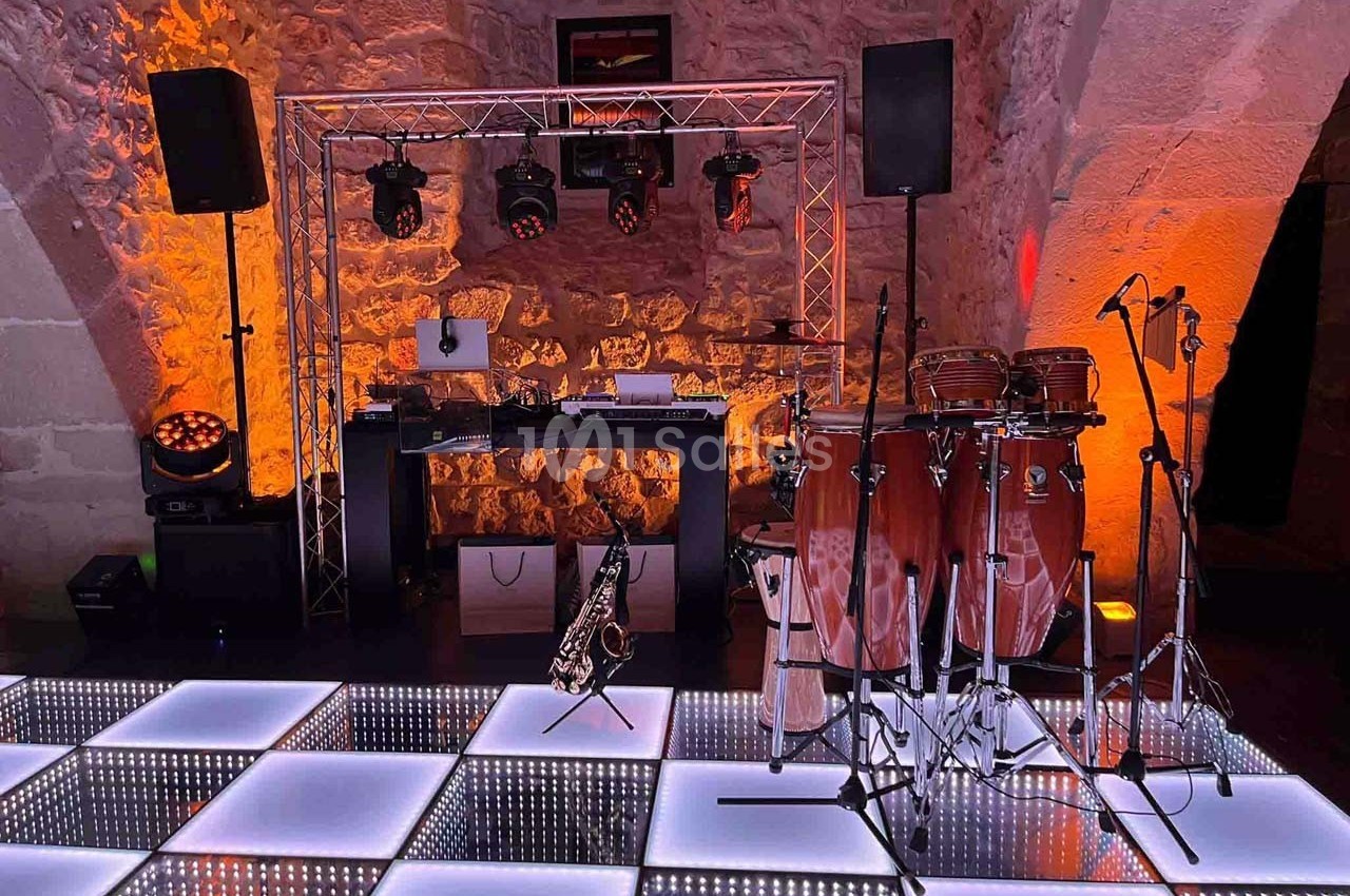 Installation musicale avec percussions, saxophone, platines DJ et éclairage coloré dans une salle en pierre voûtée.