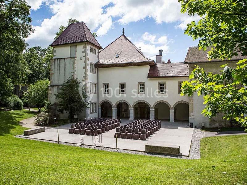 Cour extérieure d'un bâtiment historique avec des chaises disposées en rangées, entourée de verdure et d'arbres.