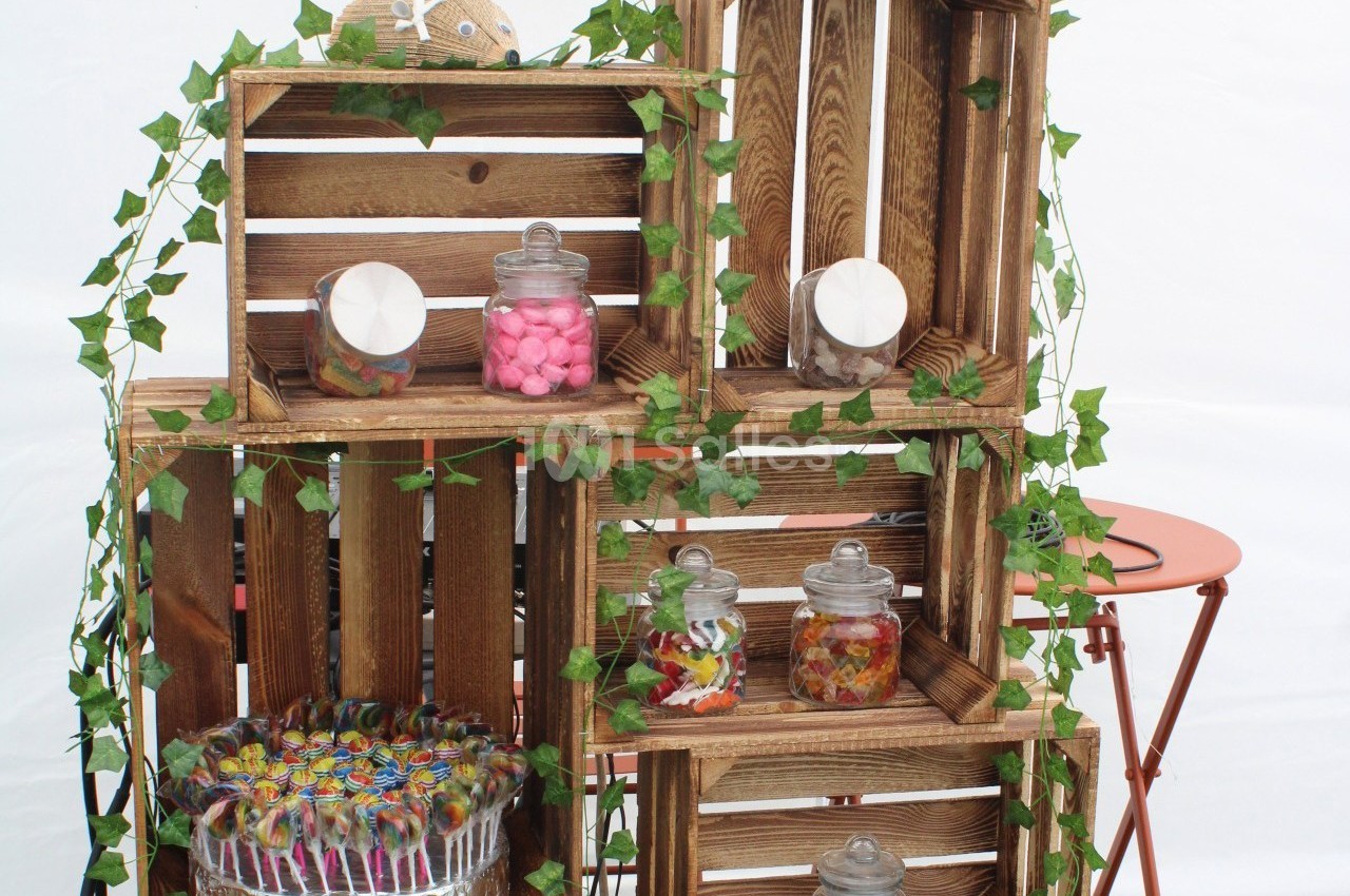 Casiers en bois empilés décorés de lierre, contenant des bocaux de bonbons colorés et un plateau de sucettes.