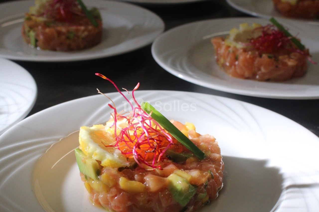 Tartare de saumon avec avocat, mangue et décoration de germes rouges, servi sur une assiette blanche.