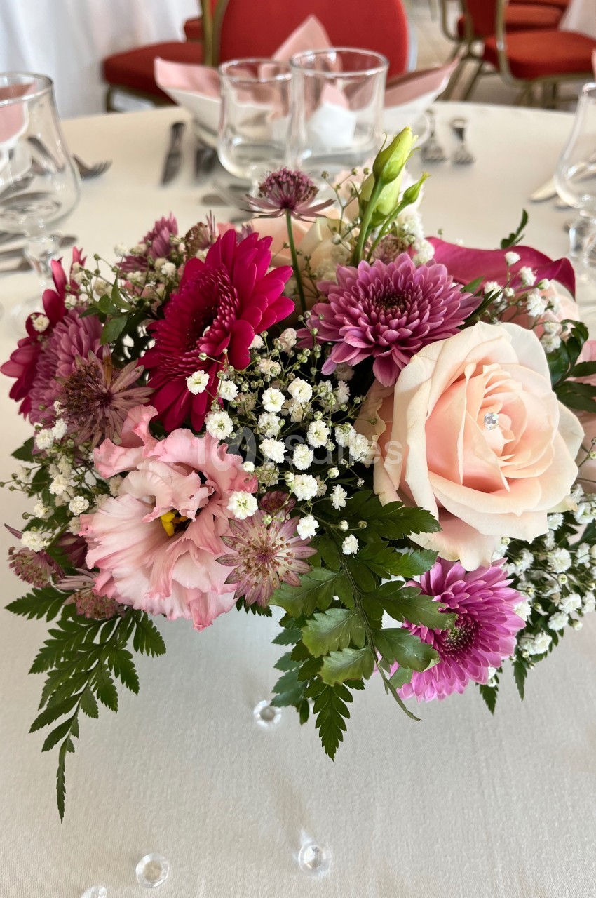 Centre de table floral avec roses roses, chrysanthèmes violets, gypsophiles blanches et feuillage vert.