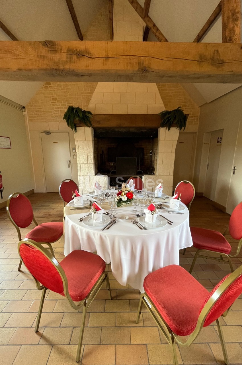 Table ronde dressée avec nappes blanches, vaisselle élégante et centre de table floral, entourée de chaises rouges.
