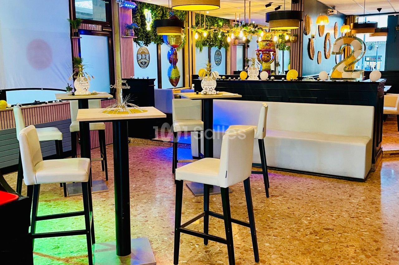 Salle lumineuse avec tables hautes, chaises blanches, décorations modernes et plantes suspendues.