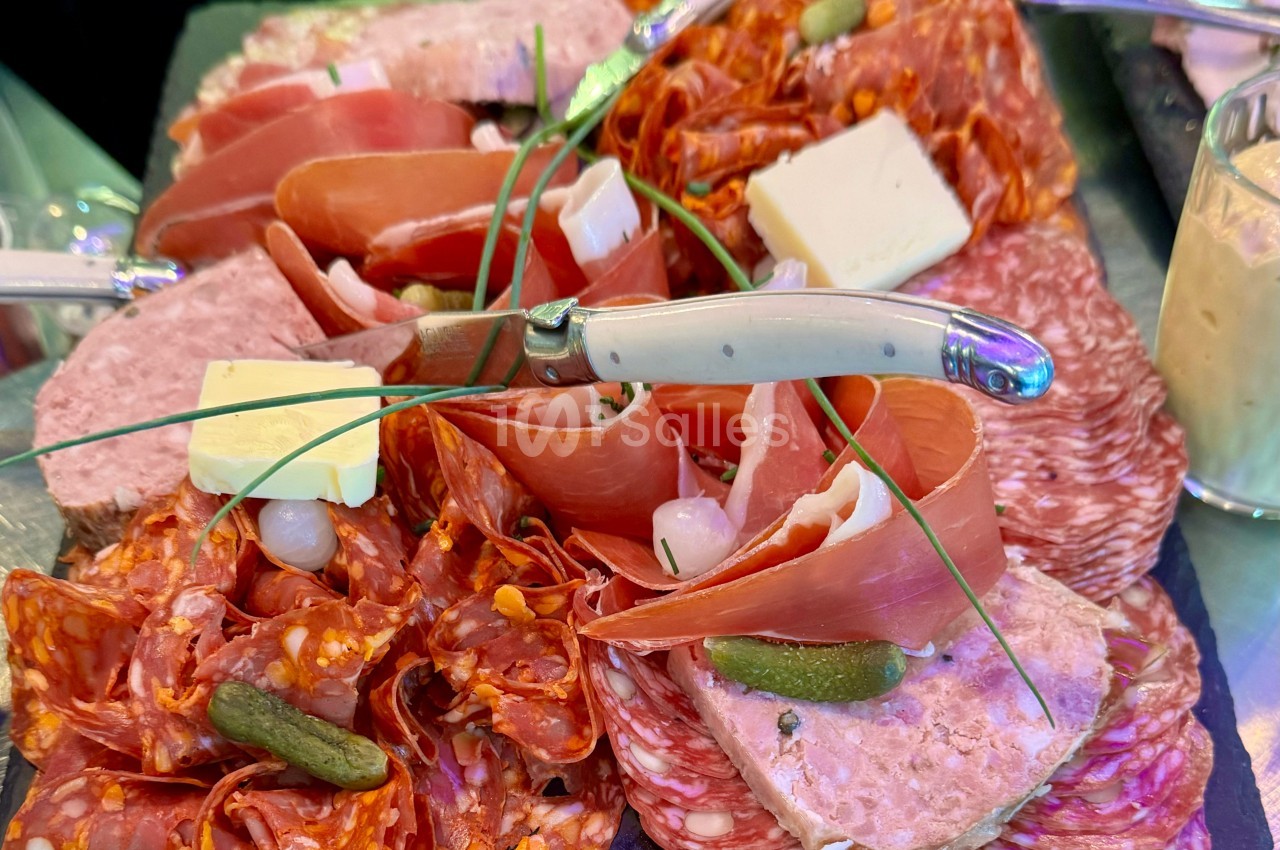 Plateau de charcuterie variée avec saucissons, jambon, pâté, cornichons, fromage et brins de ciboulette.