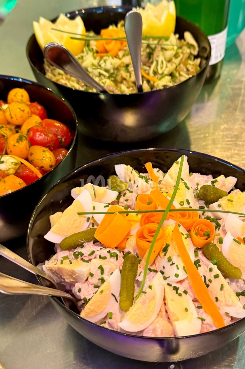 Assortiment de salades dans des bols noirs : salade de pommes de terre, tomates cerises et pâtes au pesto.